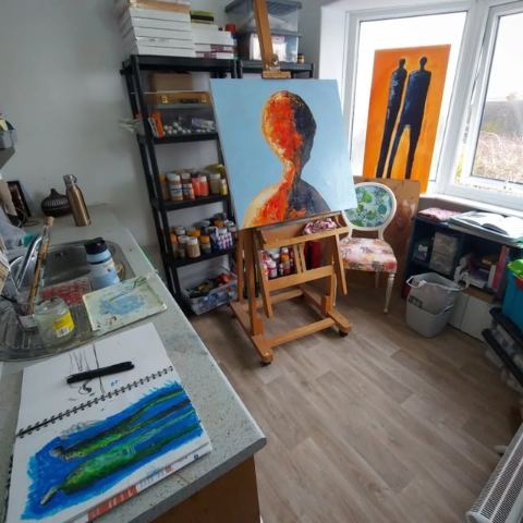 A view across Helen Morgan's studio with two finished figurative paintings and a sketchbook