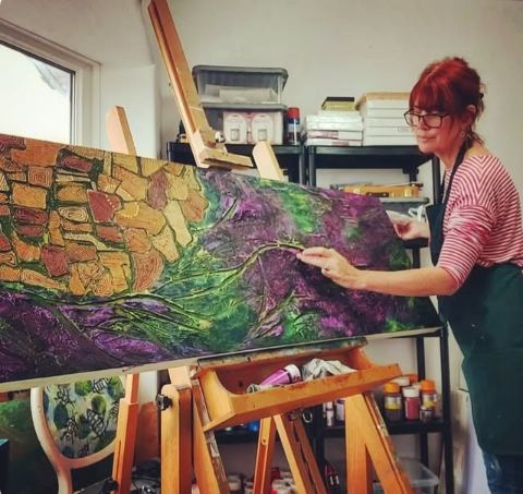 Helen Morgan working on a textured green and violet abstract landscape piece